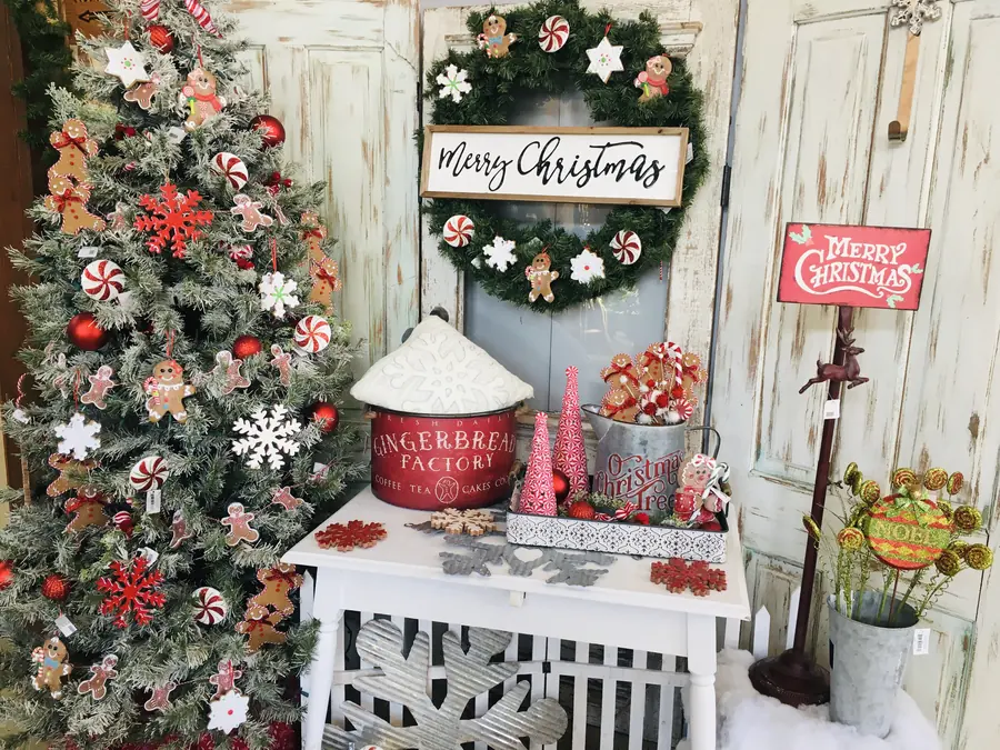 Flocked Christmas tree with red ornaments beside a Merry Christmas wreath and gingerbread decor