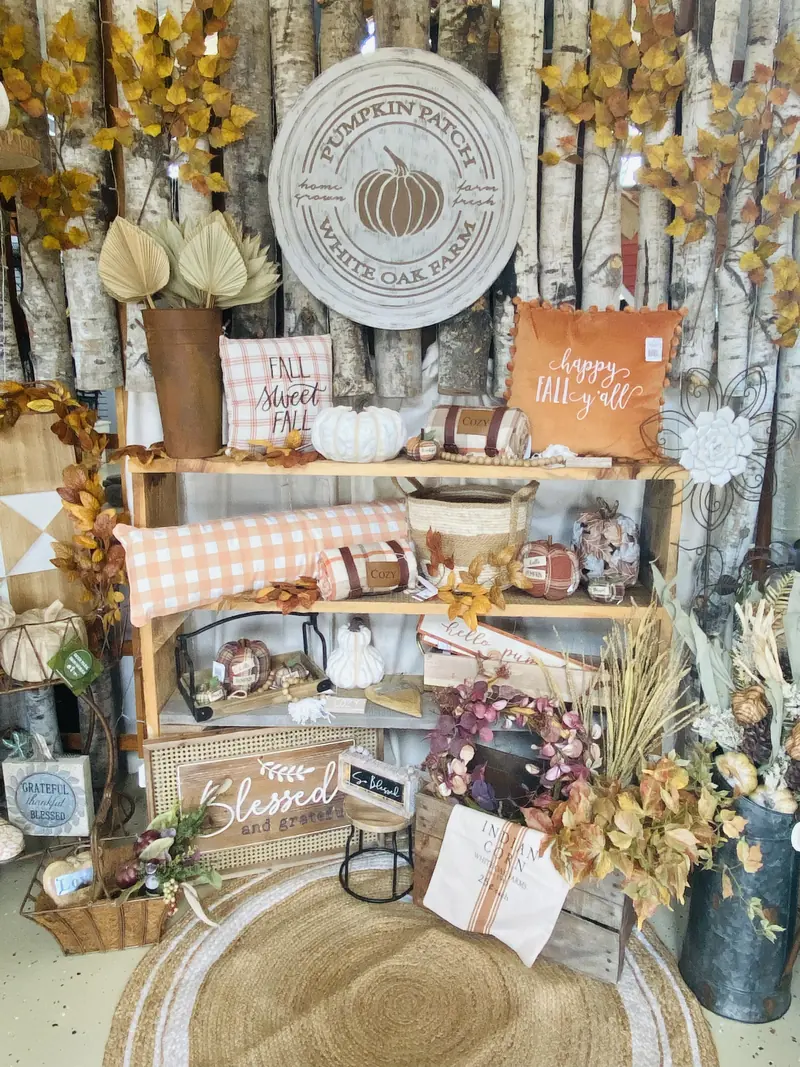 Gift shop shelves styled for fall with pumpkins, pillows, wreaths and birch logs