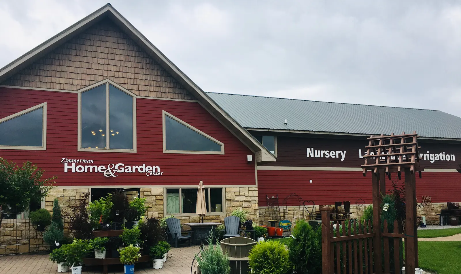 Front of Zimmerman Home and Garden Center, a red building with a green roof, nursery and landscape signs, and planted beds at the entrance